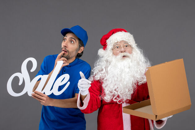 圣诞老人圣诞老人的正面图 男信使拿着卖东西的字条 灰色墙上挂着空的食品盒前面圣诞快乐服装