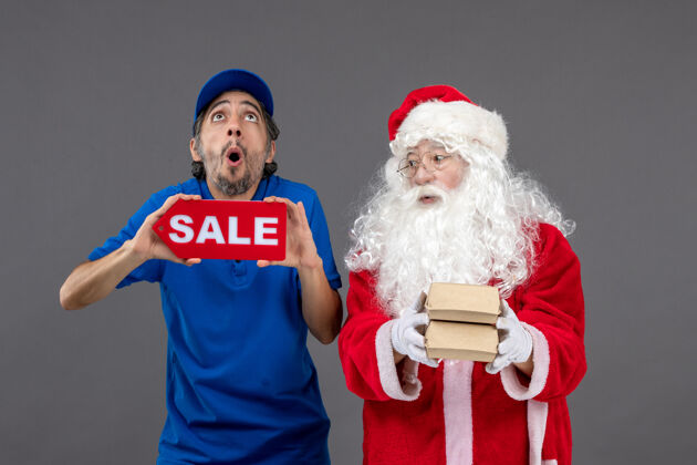 快乐圣诞老人的正面图 男信使手持销售横幅 灰色墙上有食品包装圣诞老人人销售