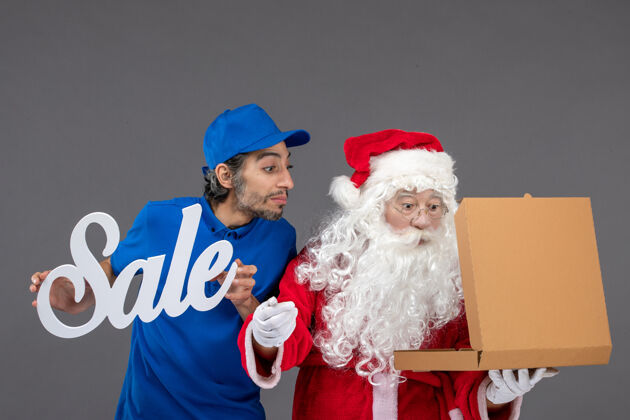 男人圣诞老人的正面图 男信使拿着卖东西的字条和灰墙上的食品盒圣诞快乐十二月圣诞老人
