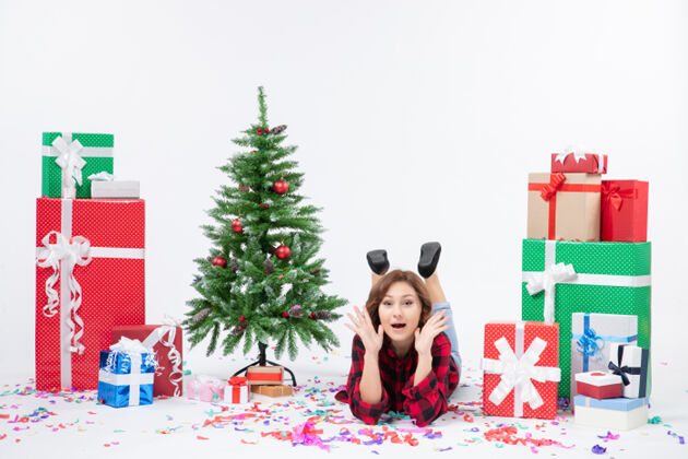 圣诞正面图年轻女性躺在白色办公桌上的圣诞礼物和圣诞树周围圣诞新年礼物颜色雪地雪树礼物