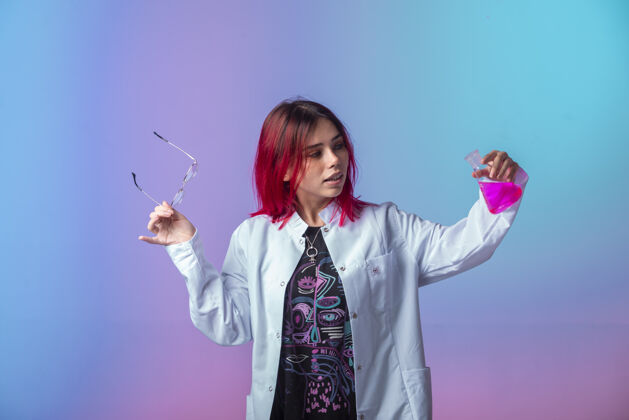 成人一个粉红色头发的年轻女孩拿着一个化学瓶 聚精会神地看着摆姿势人女性