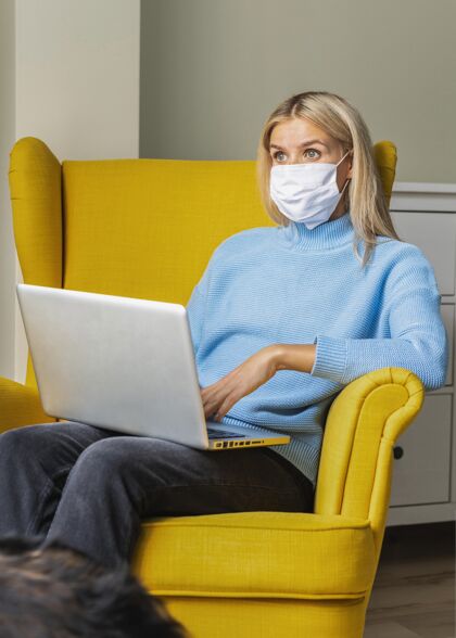 Ncov大流行期间 戴着医用口罩在家里用笔记本电脑工作的女人隔离扶手椅妇女