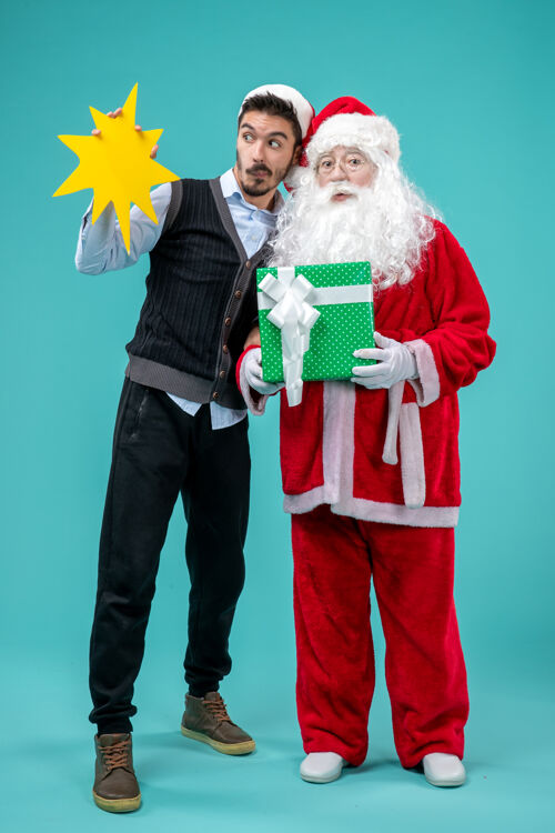 黄色前视图：圣诞老人和手持蓝色背景黄色标志的年轻男性风景圣诞老人蓝色