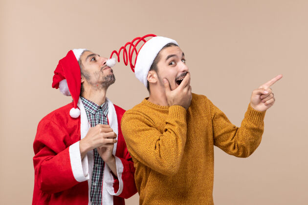 圣诞老人正面图两个戴着圣诞帽的朋友一个戴着帽子 另一个在米色背景上显示方向两个朋友朋友男人
