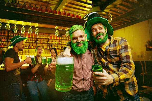 吐司圣帕特里克节聚会快乐的朋友们正在庆祝和喝绿色啤酒年轻男女戴着绿色帽子酒吧内部小妖精品脱开朗