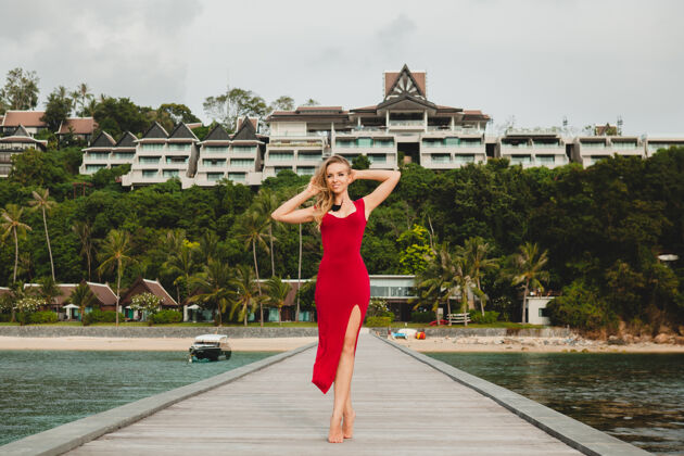 女性年轻漂亮迷人的女人独自站在豪华度假酒店的码头上 暑假 红色长裙 金色头发 性感服装 热带沙滩 诱惑 性感 微笑度假胜地魅力连衣裙