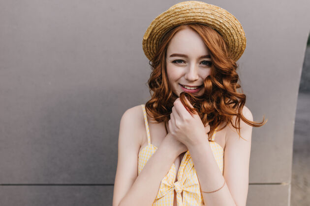 配件戴着帽子的顽皮的白人女孩微笑着站在灰色的墙上 看着她幽默的女模特抚摸着她的红发的肖像漂亮人姜黄色