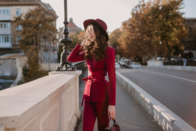 时尚可爱漂亮的时尚女人穿着紫色西装走在城市的大街上 春夏秋冬时节时尚潮流戴着帽子 拿着钱包深色漂亮服装