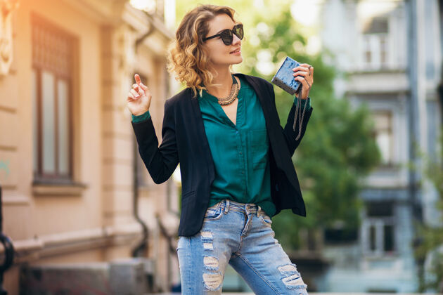 穿着时尚写真的年轻优雅的女人走在街上穿着黑色夹克 绿色衬衫 时尚配饰 拿着小钱包 戴着墨镜 夏日街头时尚风格手提包肖像包