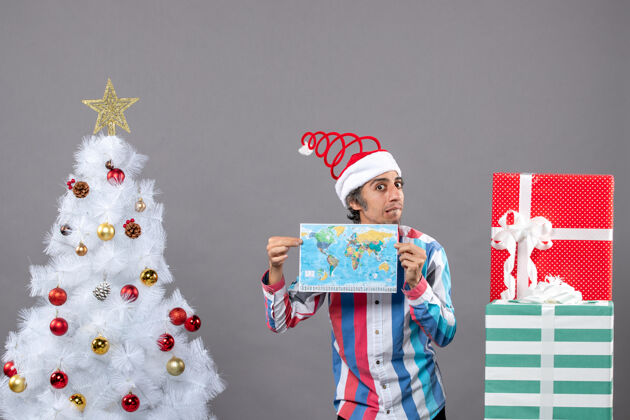 地球前视图失望的男子与螺旋弹簧圣诞老人帽子举行地图与双手地球仪礼品盒圣诞老人