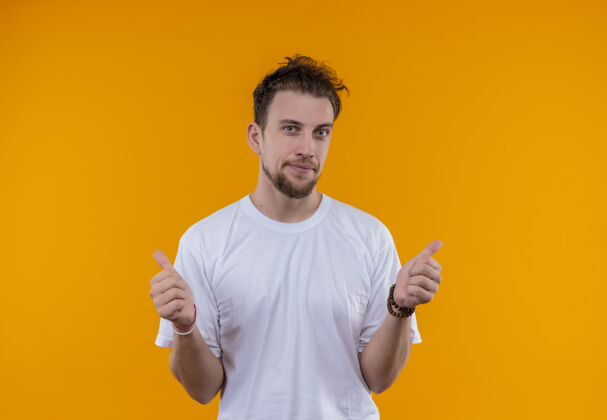 小伙子穿着白色t恤的年轻人很高兴 他在孤立的橙色背景上竖起大拇指白色向上拇指