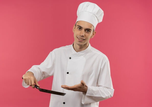 分面带微笑的年轻男厨师身穿厨师制服 手捧并用手指着有复印空间的煎锅平底锅手厨师