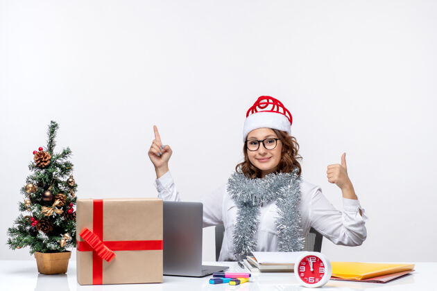 白色正面图：年轻的女工坐在白色背景的工作场所前圣诞节桌子电脑