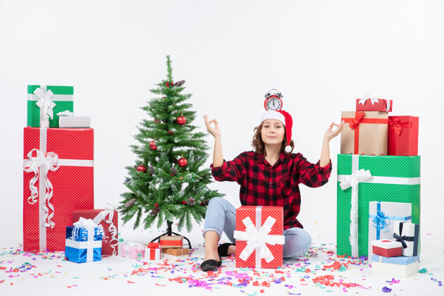 圣诞节一位年轻女子坐在一堵白墙上 头上拿着钟 围着礼物转节日人十二月