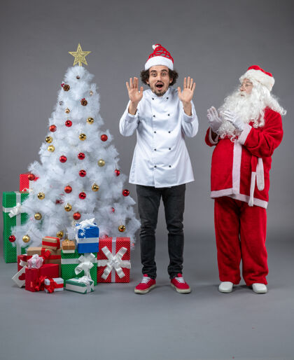 冬天圣诞老人和男厨师在灰色墙上围着圣诞礼物的正视图快乐溜冰圣诞老人