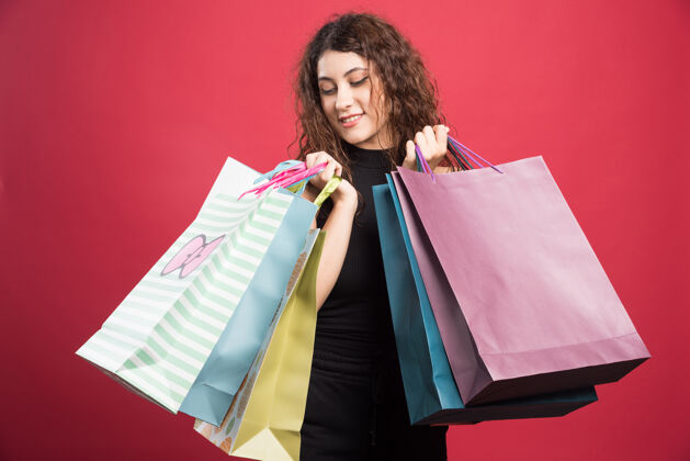 购物在红色背景上展示新买衣服的女士高质量照片购买购物女孩