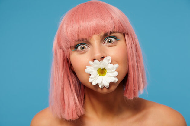 姿势一个年轻漂亮的粉红色头发的女人 留着短发 围着她绿色的眼睛看镜头 站在蓝色的背景上 嘴里叼着白色的花积极20秒箭