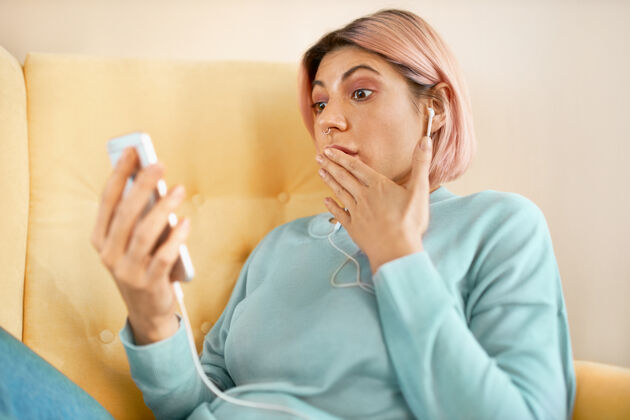 沙发情绪激动的小红发女子坐在沙发上拿着智能手机 惊讶地捂着嘴女人短信生活