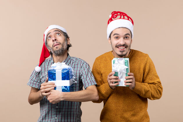 肖像正面图两个家伙一个高高地看着另一个微笑着拿着他们的礼物在米色孤立的背景视图男微笑