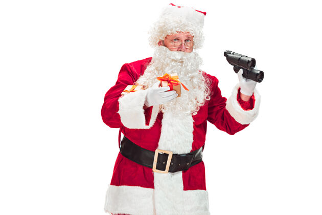 望远镜一个穿着圣诞老人服装的人的肖像-有一个豪华的白胡子 圣诞老人的帽子和一个红色的服装-在一个白色的背景上用望远镜孤立的全长圣诞节圣诞老人男性