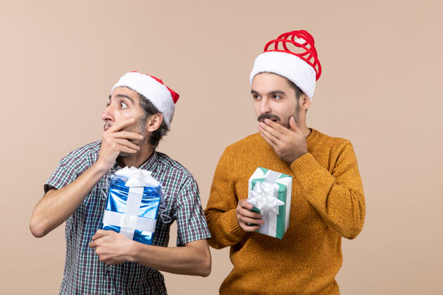 成人正面图两个流浪汉手捂嘴 拿着圣诞礼物 背景是米色的流浪圣诞节男人