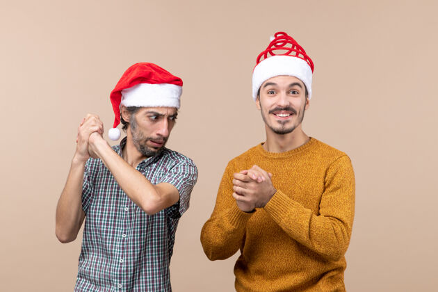 男人正面图两个戴着圣诞帽的男人手牵手在米色孤立的背景上男人两个男人帽子