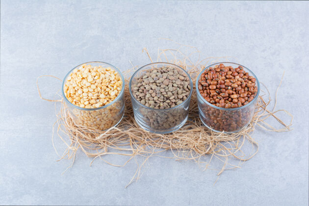 农业各种各样的豆科植物放在玻璃碗里 放在大理石背景上的一堆稻草上豆类配料豆类