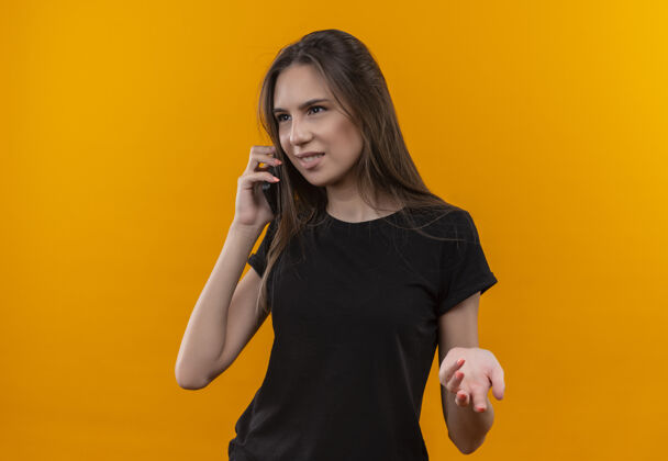 电话看着身边穿着黑色t恤的年轻白人女孩在孤立的橙色背景下讲电话说话女孩看