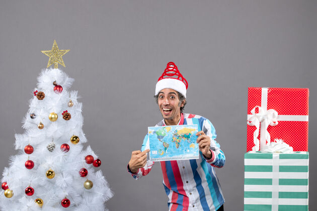 假期正面图：戴着螺旋弹簧圣诞帽的快乐男人指着世界地图地图人礼物