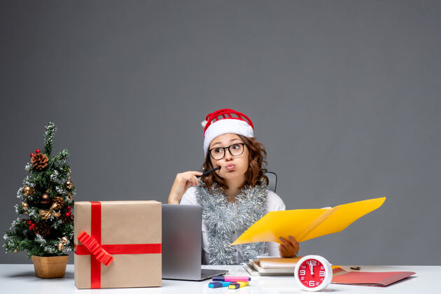 圣诞节前视图年轻的女工人坐在她的位置前 在灰色背景下处理文件工作电脑文件