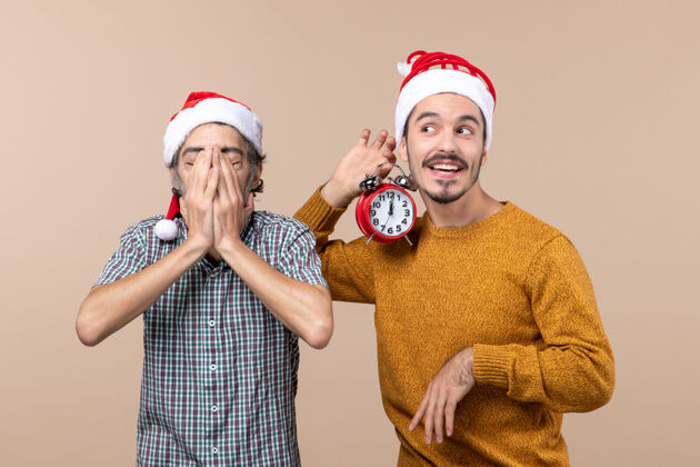 视图前视图两个圣诞老人一个用手捂住脸 另一个拿着闹钟 背景是米色的前面闹钟男人