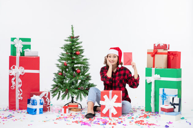 快乐前视图年轻女子坐在周围的礼物举行信封上的白墙前面雪礼物