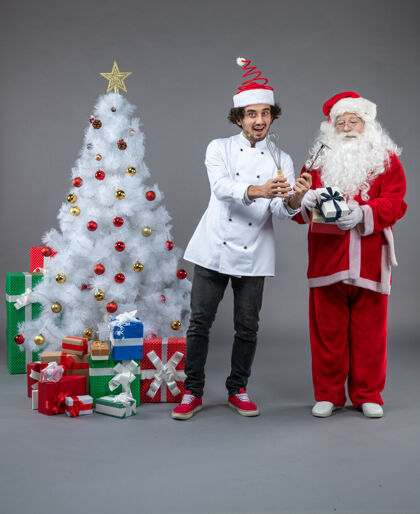 圣诞快乐圣诞老人和男厨师在灰色墙上围着圣诞礼物的正视图快乐前面圣诞