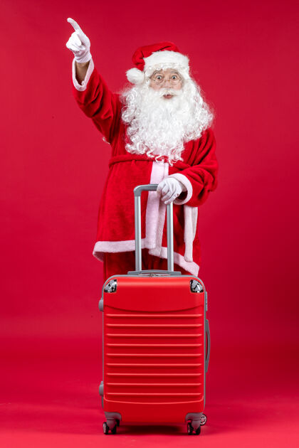 十二月圣诞老人的正面图 红色的墙上挂着他的红色袋子人手推车圣诞老人