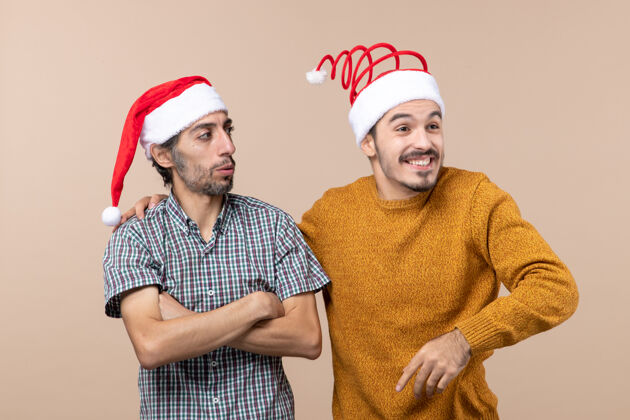 男人正面图两个戴圣诞帽的家伙一个把手放在另一个肩膀上 在孤立的背景下微笑手微笑前面