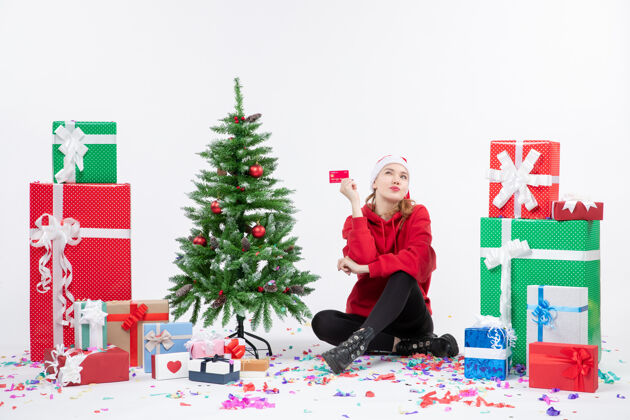节日正面图：年轻女子围坐在白墙上 手里拿着红色的银行卡人礼物圣诞快乐