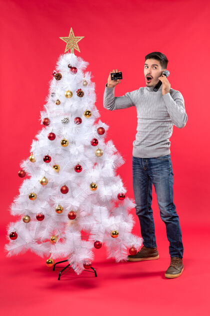 圣诞圣诞气氛 年轻人站在装饰好的圣诞树旁 拿着麦克风和电话 看起来很惊讶微笑麦克风站着