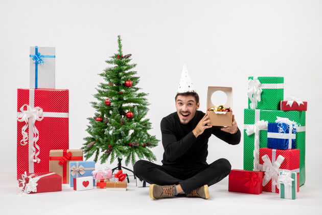 十二月正面图：年轻人围坐在白色的墙上 手里拿着圣诞礼物圣诞树人新郎