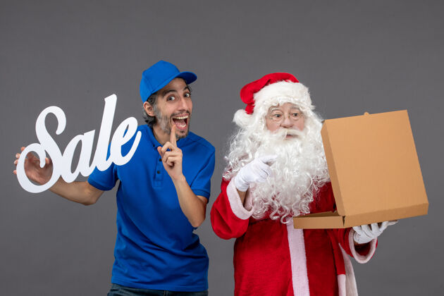 圣诞老人圣诞老人的正面图 男信使拿着卖东西的字条和灰墙上的食品盒十二月举行圣诞老人