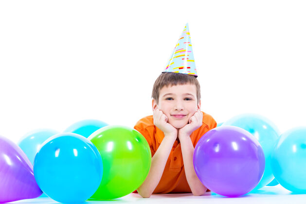 休闲穿着橙色t恤的快乐微笑男孩躺在地板上 手里拿着五颜六色的气球 竖起大拇指——孤立在白色的地板上男孩玩积极