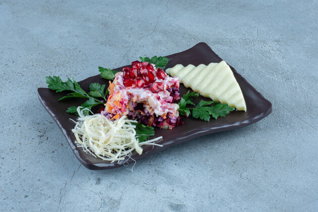石榴色拉配切片和磨碎的奶酪放在大理石上的黑色盘子里沙拉晚餐奶酪