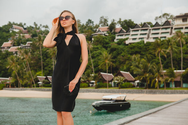 休闲奢华性感迷人的女人穿着黑色礼服在豪华度假酒店的码头上摆造型 戴着墨镜 暑假 热带海滩女士帆船摆姿势