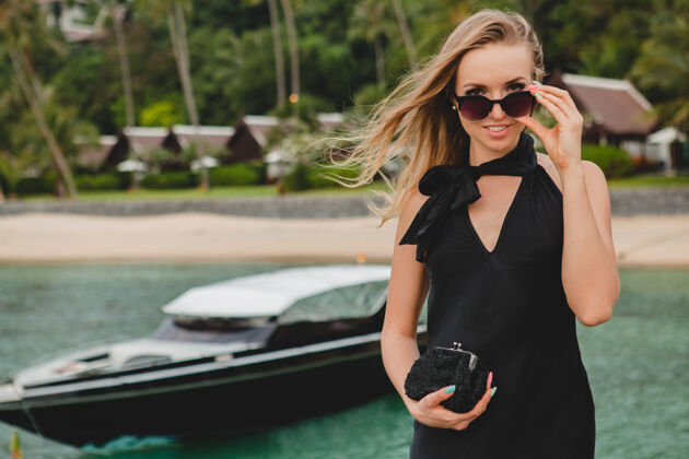 海洋奢华性感迷人的女人穿着黑色礼服在豪华度假酒店的码头上摆造型 戴着墨镜 暑假 热带海滩时尚人豪华