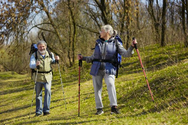 在一起在阳光明媚的日子里 一对身着旅游服装的老年夫妇在小溪边的绿色草坪上散步旅游理念 健康的生活方式 放松和团聚退休老年人游客