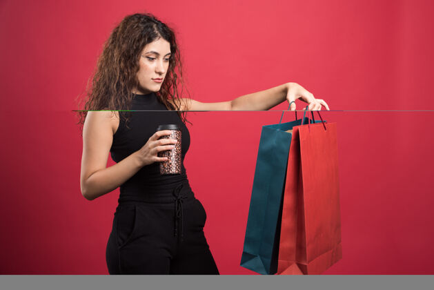 人一个拿着杯子的女人在展示她的两袋红色背景的新衣服买购物年轻