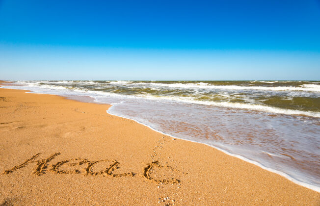 夏季在阳光明媚温暖的夏日里 在风浪汹涌的海浪旁的沙滩上题写着夏天期待已久的暑假和假期的概念天堂海洋美丽