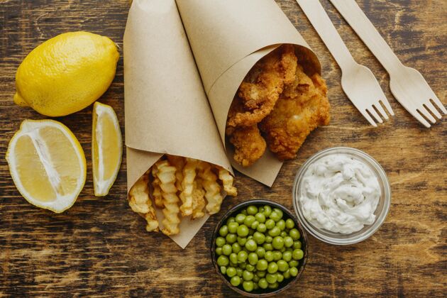水平用豌豆和刀叉纸包起来的鱼和薯条的俯视图英国土豆柠檬