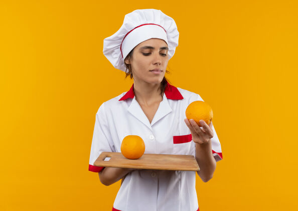 思考想着年轻的女厨师穿着厨师制服拿着橘子看着砧板上有复印空间板子厨师厨师