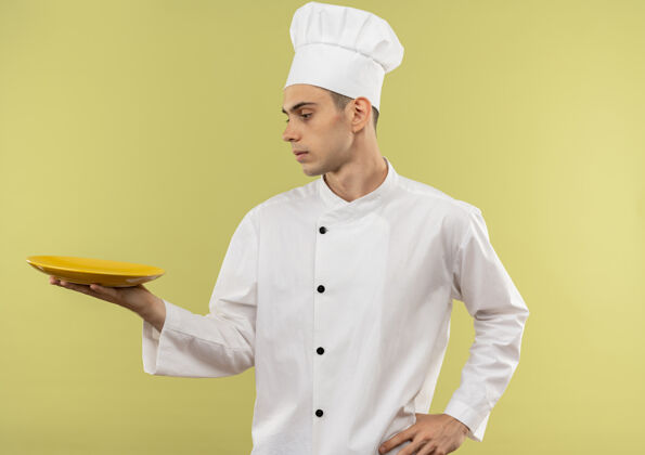 厨师站在侧视图年轻的男厨师穿着厨师制服看他的手把他的手放在臀部与复制空间板手厨师男