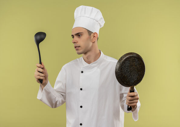 穿着想着年轻的男厨师穿着厨师制服拿着煎锅看着手中的勺子厨师制服思考